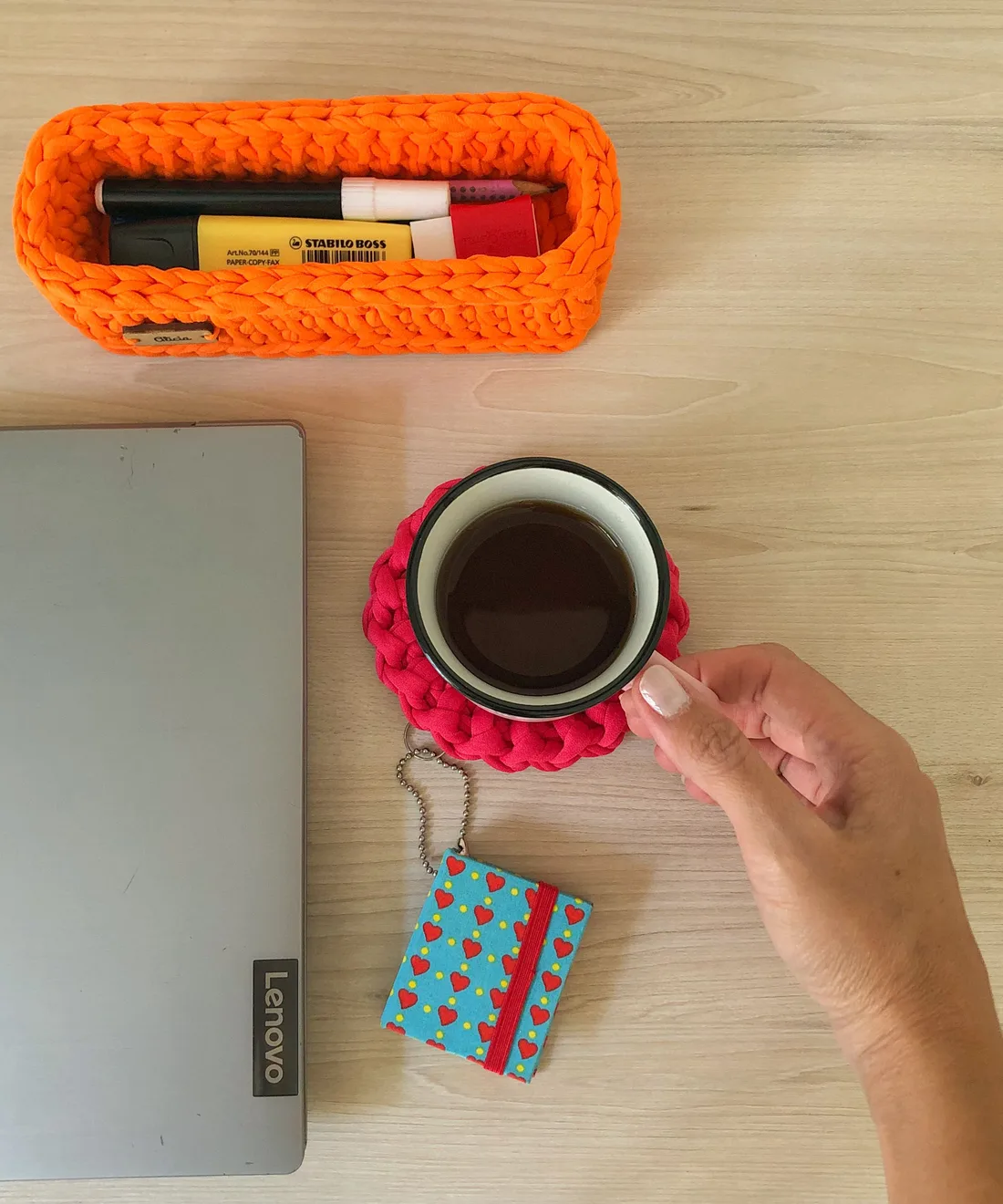 Espace de travail chaleureux : une main tient une tasse de café posée à côté d'un ordinateur portable et d'un panier de feutres